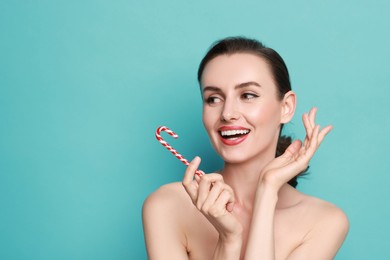 Photo of Smiling woman with perfect makeup holding Christmas candy cane on light blue background. Space for text