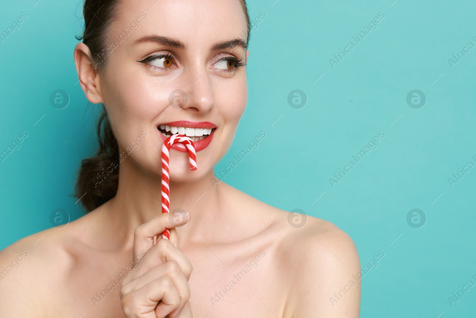 Photo of Smiling woman with perfect makeup holding Christmas candy cane on light blue background. Space for text