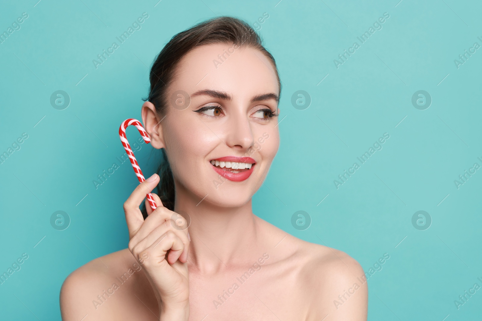 Photo of Smiling woman with perfect makeup holding Christmas candy cane on light blue background