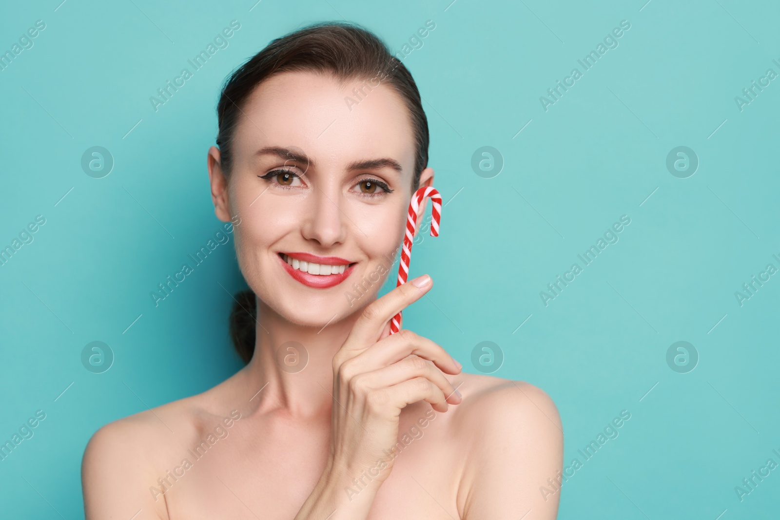 Photo of Smiling woman with perfect makeup holding Christmas candy cane on light blue background. Space for text