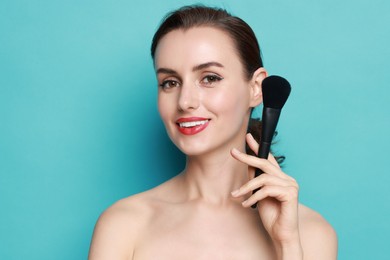 Photo of Smiling woman with makeup brush on light blue background