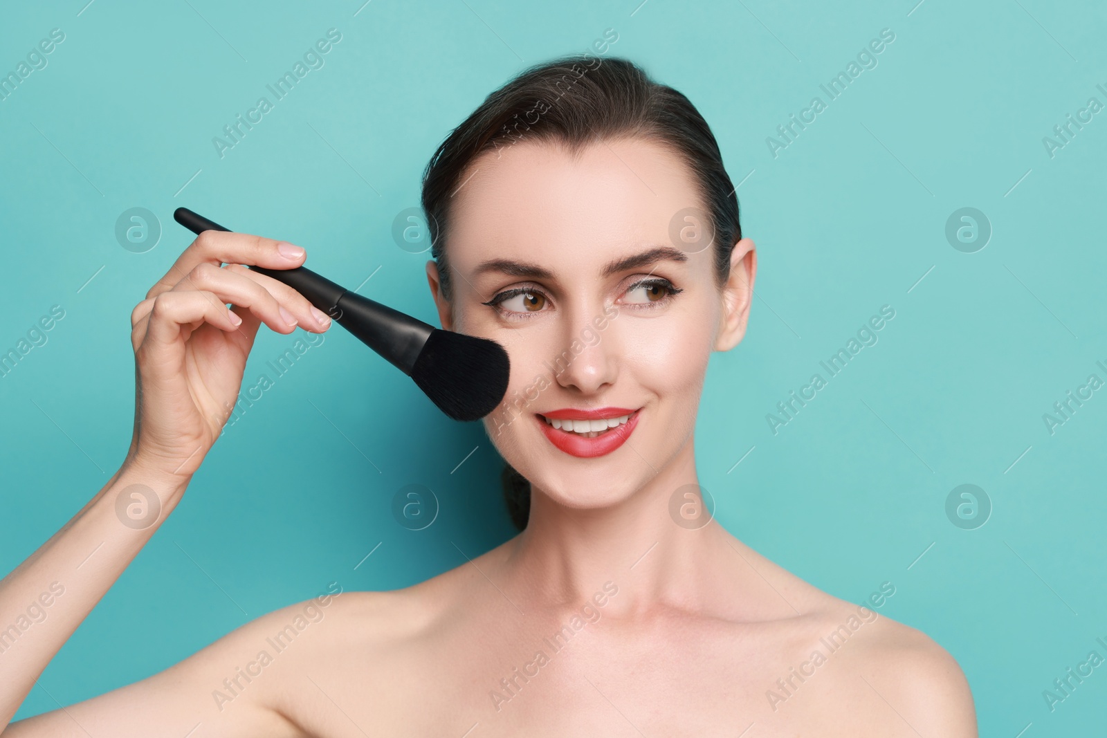 Photo of Smiling woman with makeup brush on light blue background