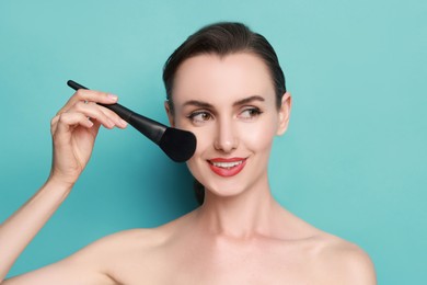 Photo of Smiling woman with makeup brush on light blue background