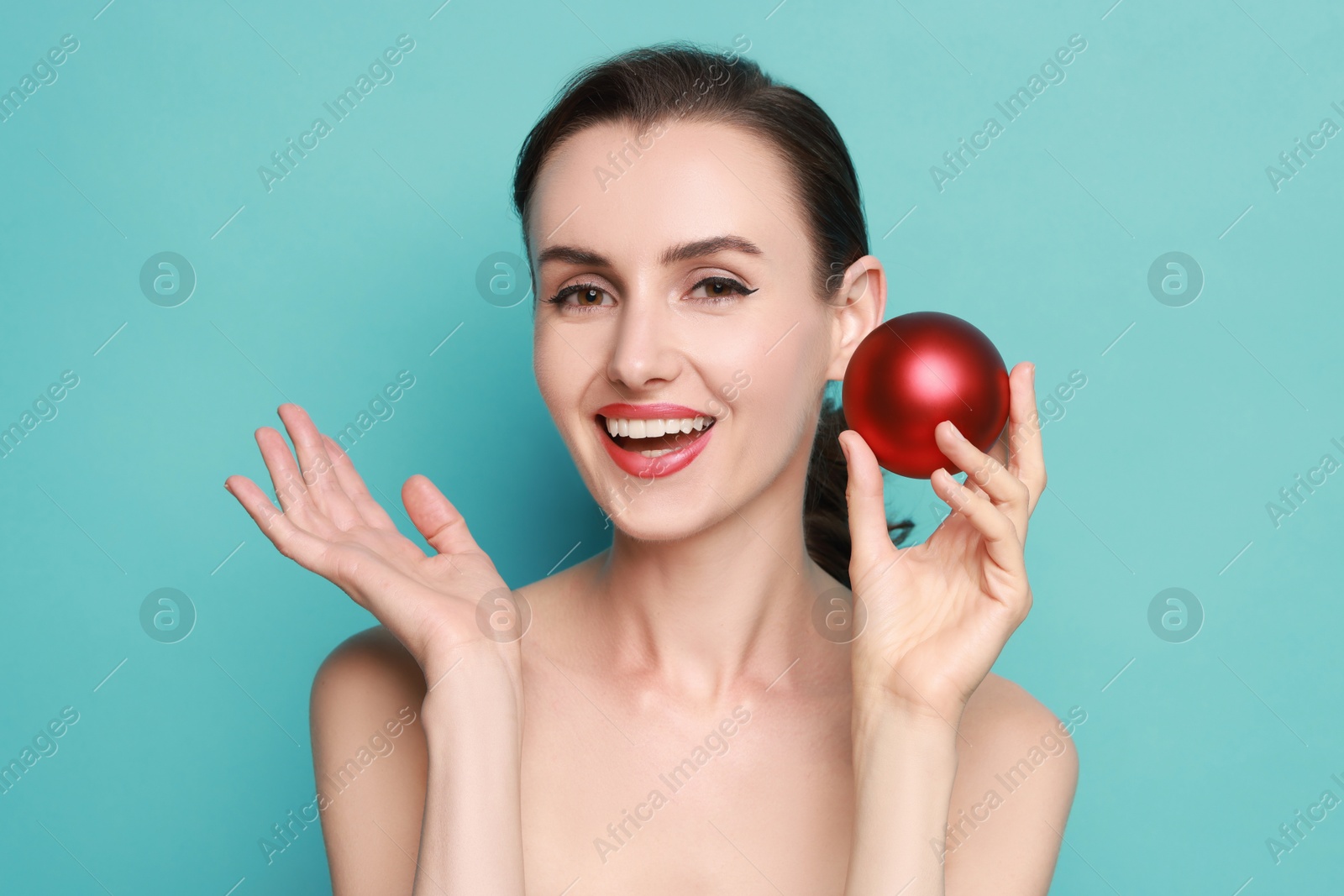 Photo of Smiling woman with perfect makeup holding Christmas bauble on light blue background