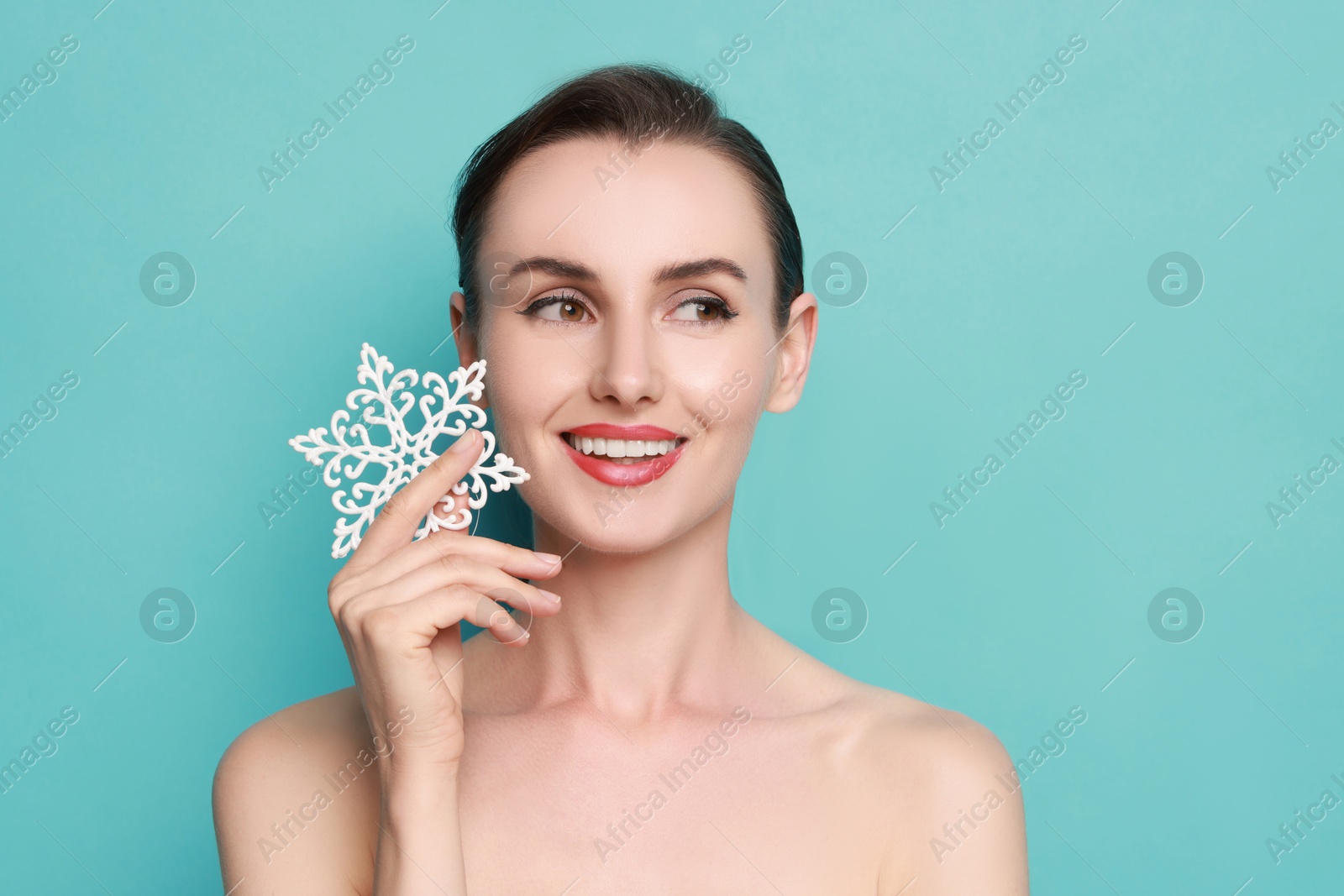 Photo of Smiling woman with perfect makeup holding decorative snowflake on light blue background. Christmas celebration