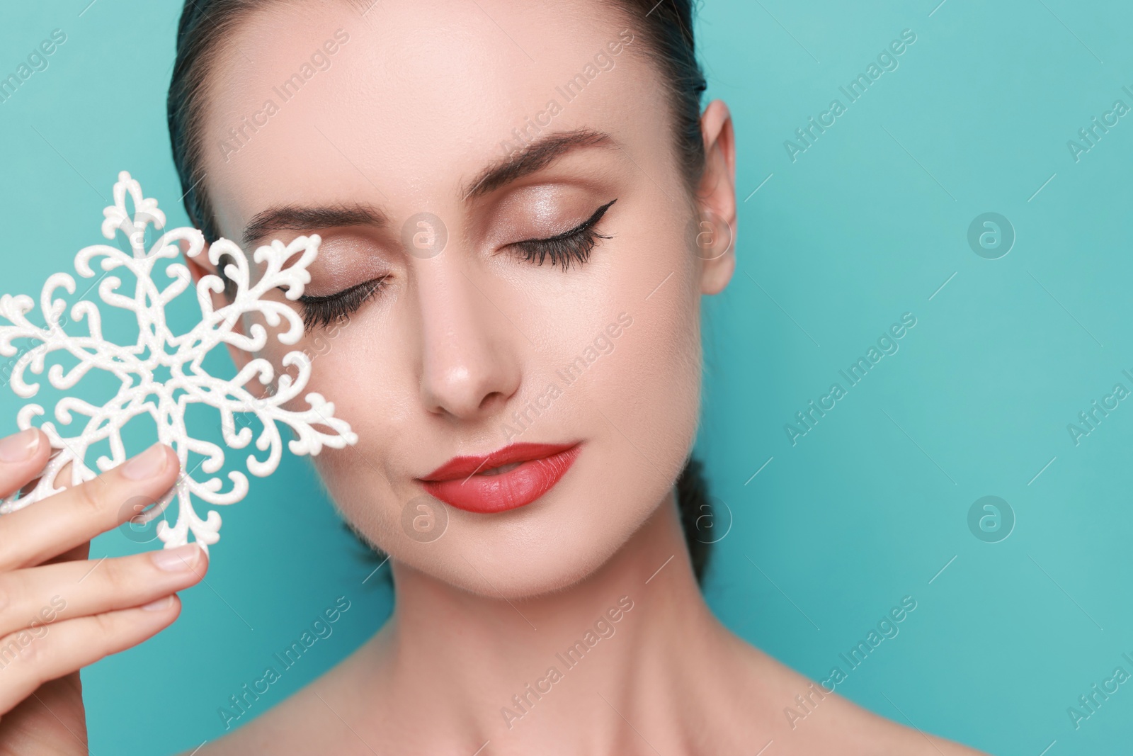 Photo of Woman with perfect makeup holding decorative snowflake on light blue background, space for text. Christmas celebration