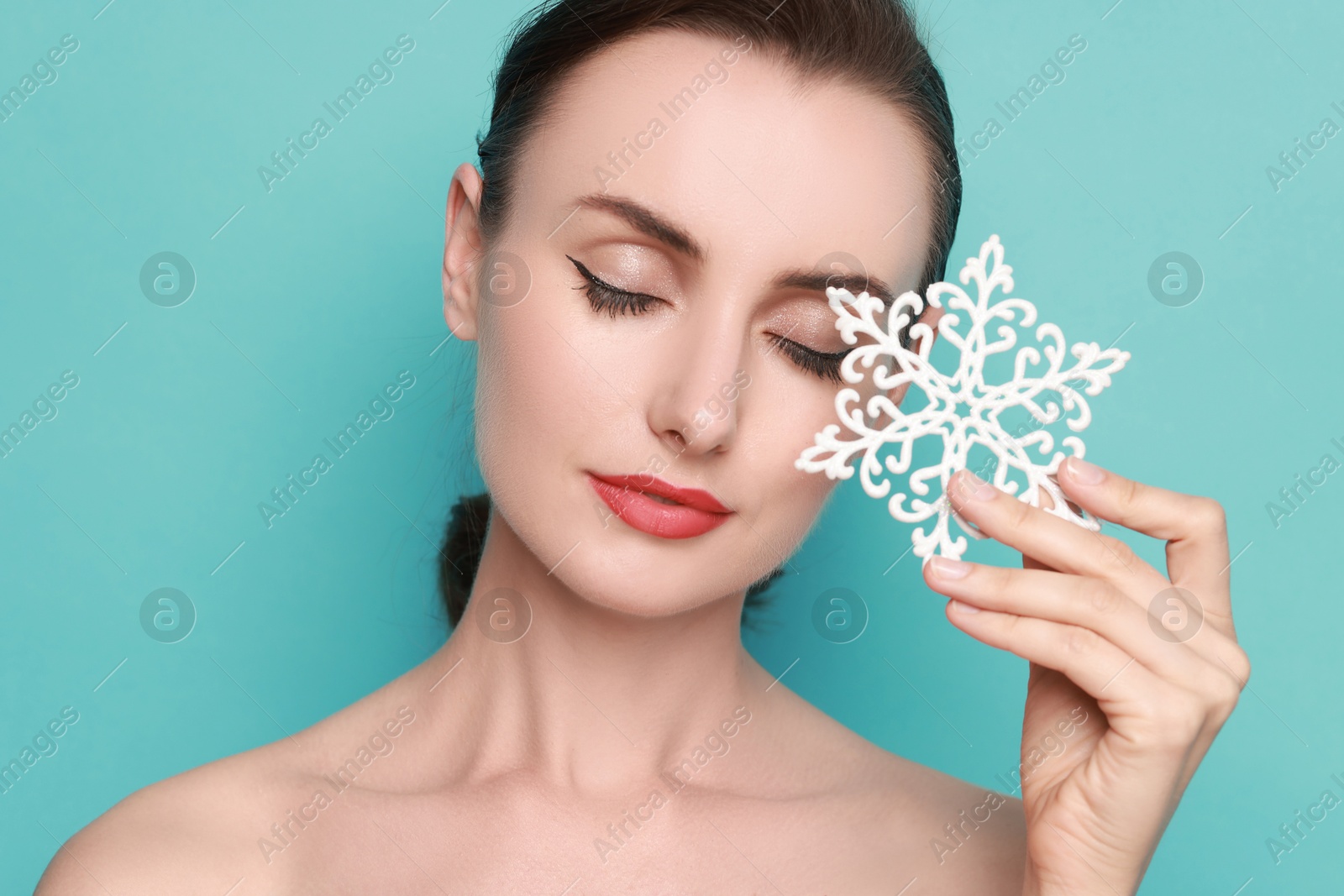 Photo of Woman with perfect makeup holding decorative snowflake on light blue background. Christmas celebration