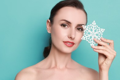 Photo of Woman with perfect makeup holding decorative snowflake on light blue background. Christmas celebration