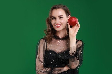 Photo of Smiling woman with perfect makeup holding Christmas bauble on green background