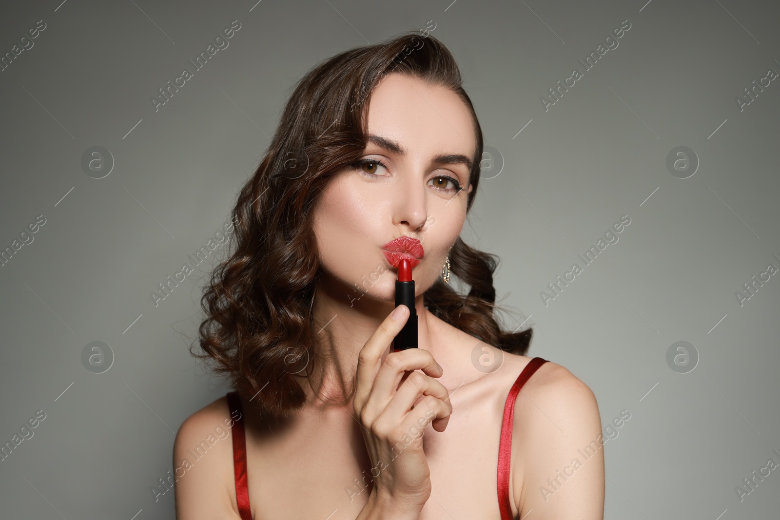 Photo of Beautiful woman applying red lipstick on grey background