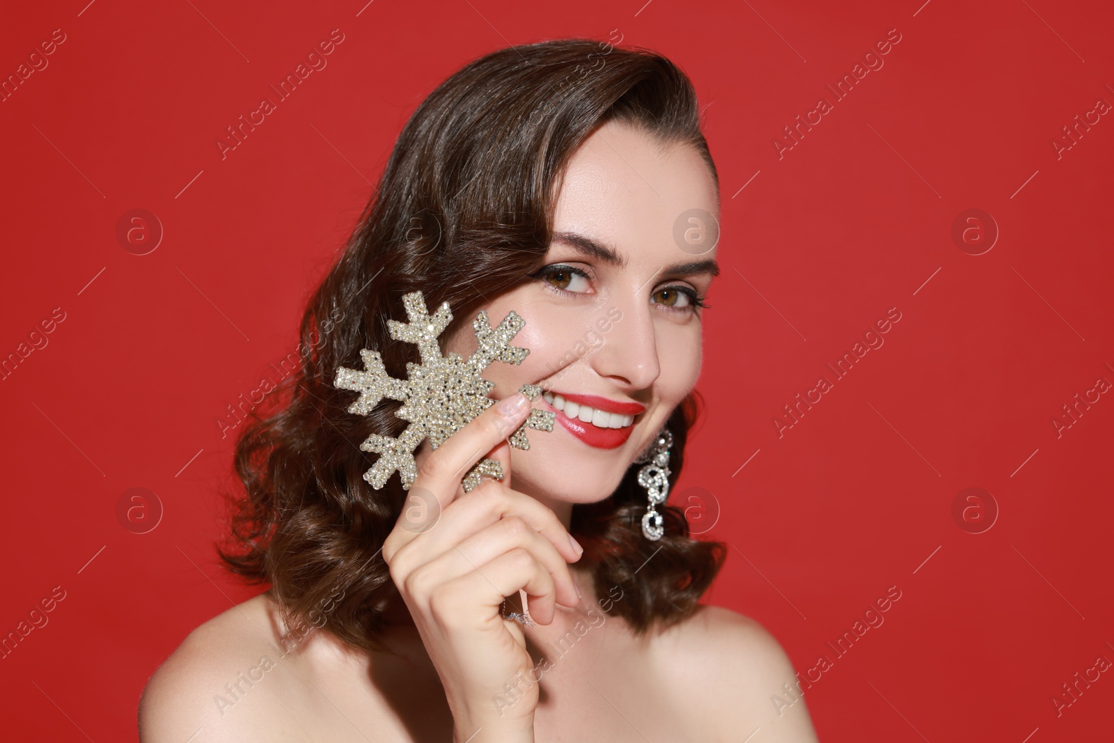 Photo of Smiling woman with perfect makeup holding decorative snowflake on red background. Christmas celebration