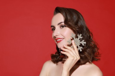 Photo of Smiling woman with perfect makeup holding decorative snowflake on red background, space for text. Christmas celebration