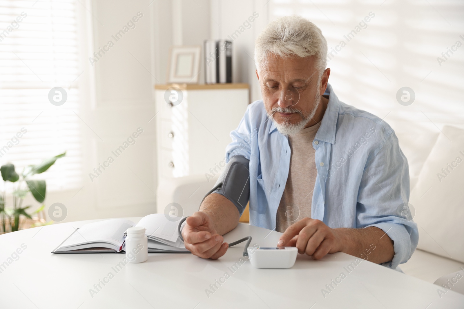 Photo of Senior man measuring blood pressure at table indoors