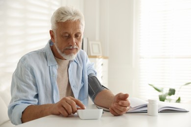 Photo of Senior man measuring blood pressure at table indoors