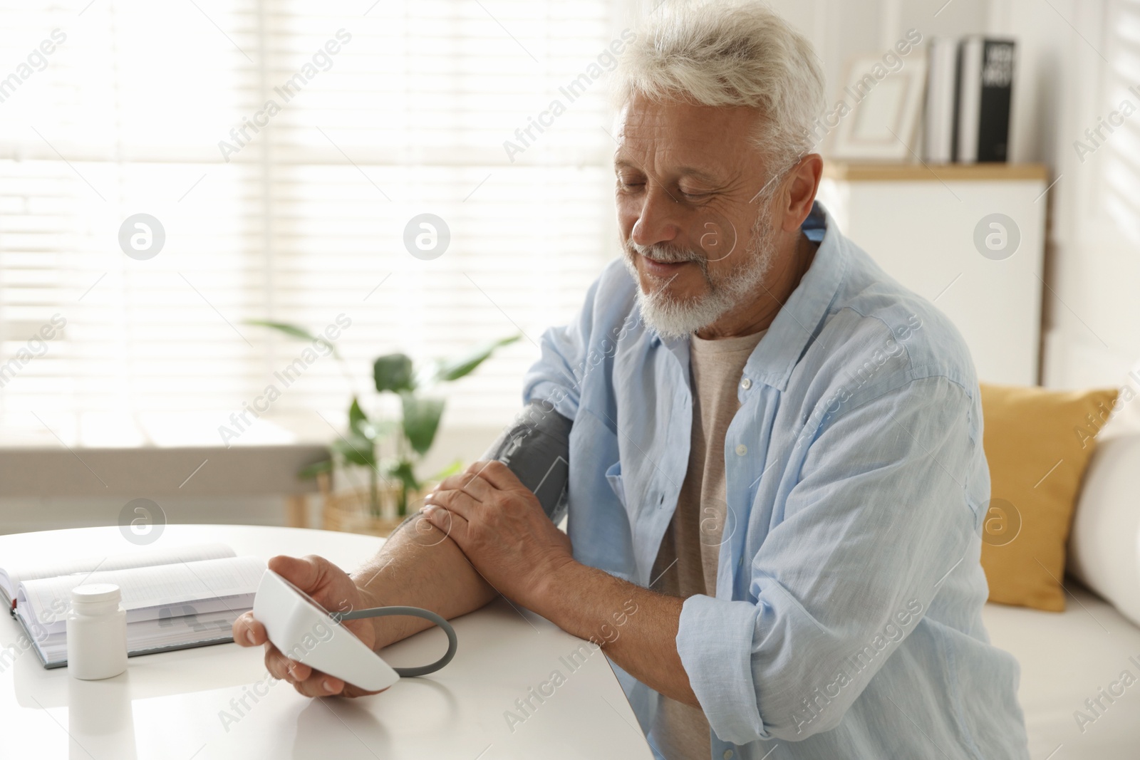 Photo of Senior man measuring blood pressure at table indoors