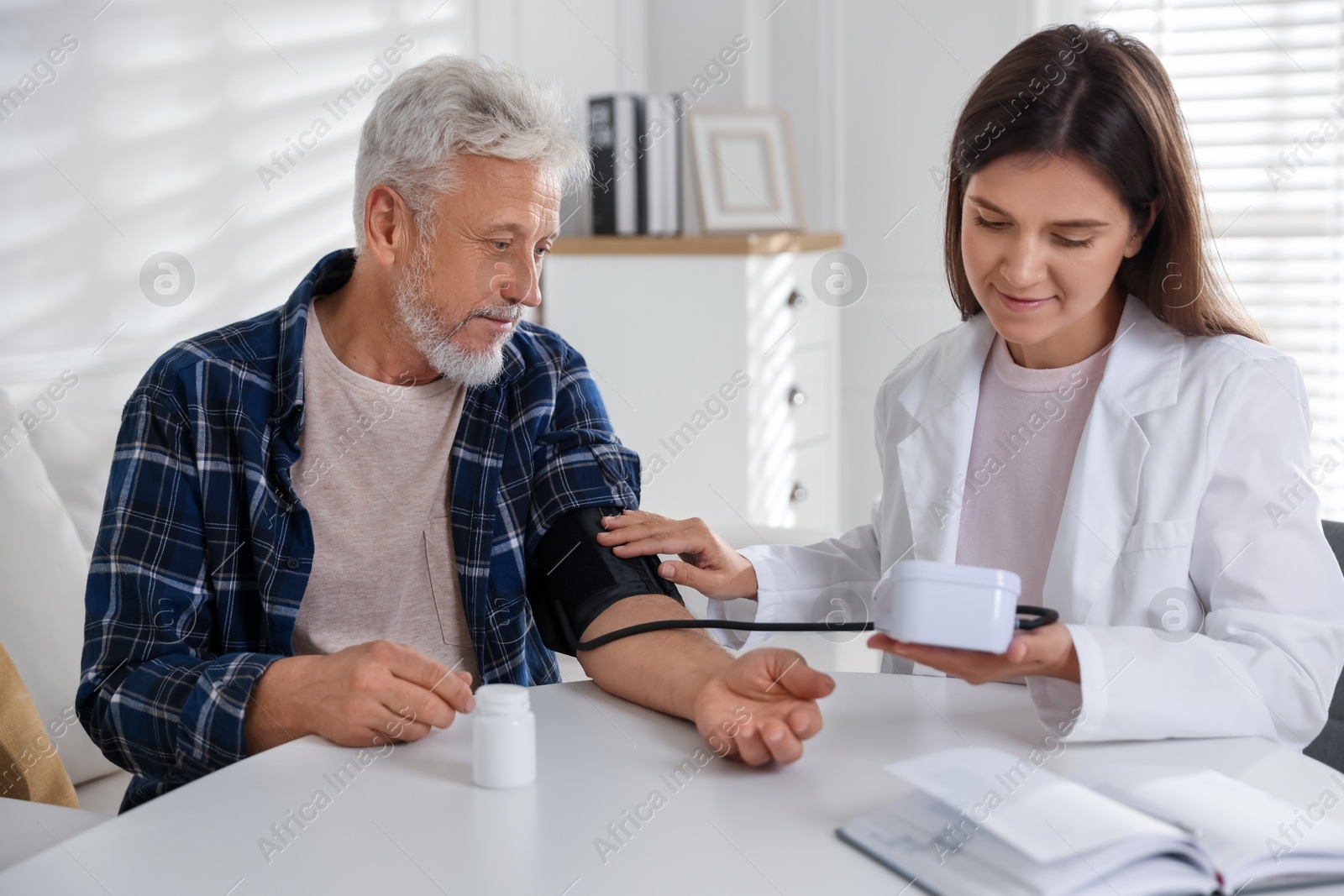 Photo of Doctor measuring patient's blood pressure at table in hospital