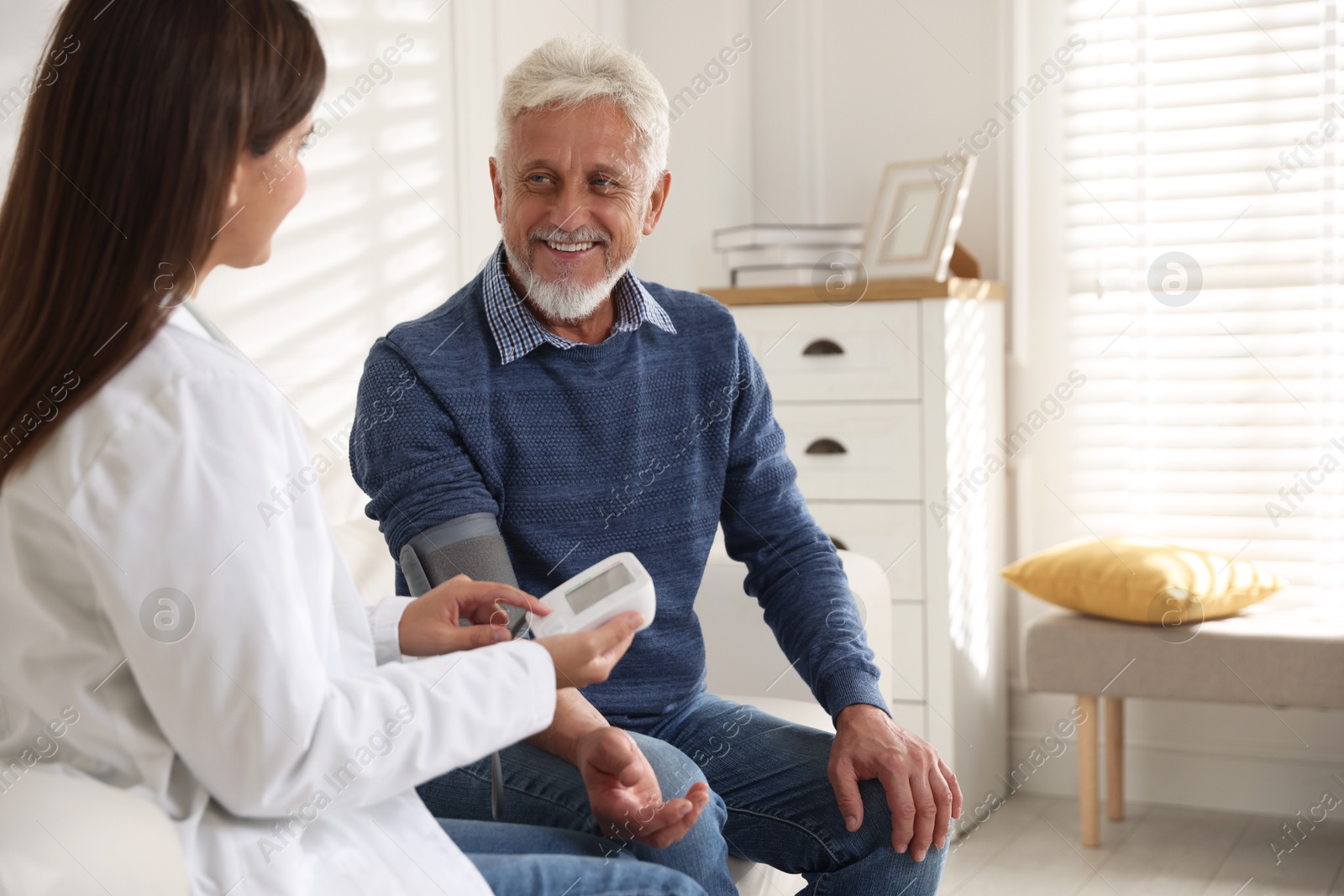 Photo of Doctor measuring patient's blood pressure on sofa indoors