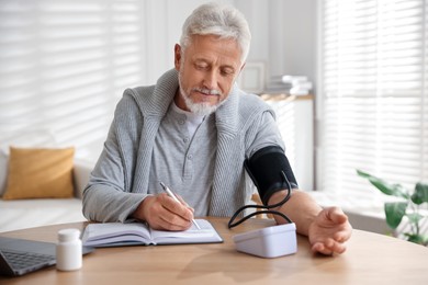 Photo of Senior man measuring blood pressure at wooden table indoors