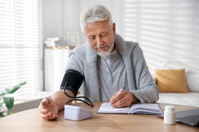 Photo of Senior man measuring blood pressure at wooden table indoors