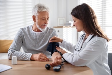 Doctor measuring patient's blood pressure at table indoors