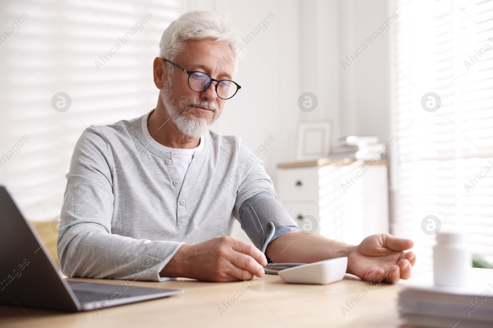 Photo of Senior man measuring blood pressure at table indoors