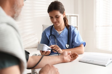 Photo of Doctor measuring patient's blood pressure at table indoors