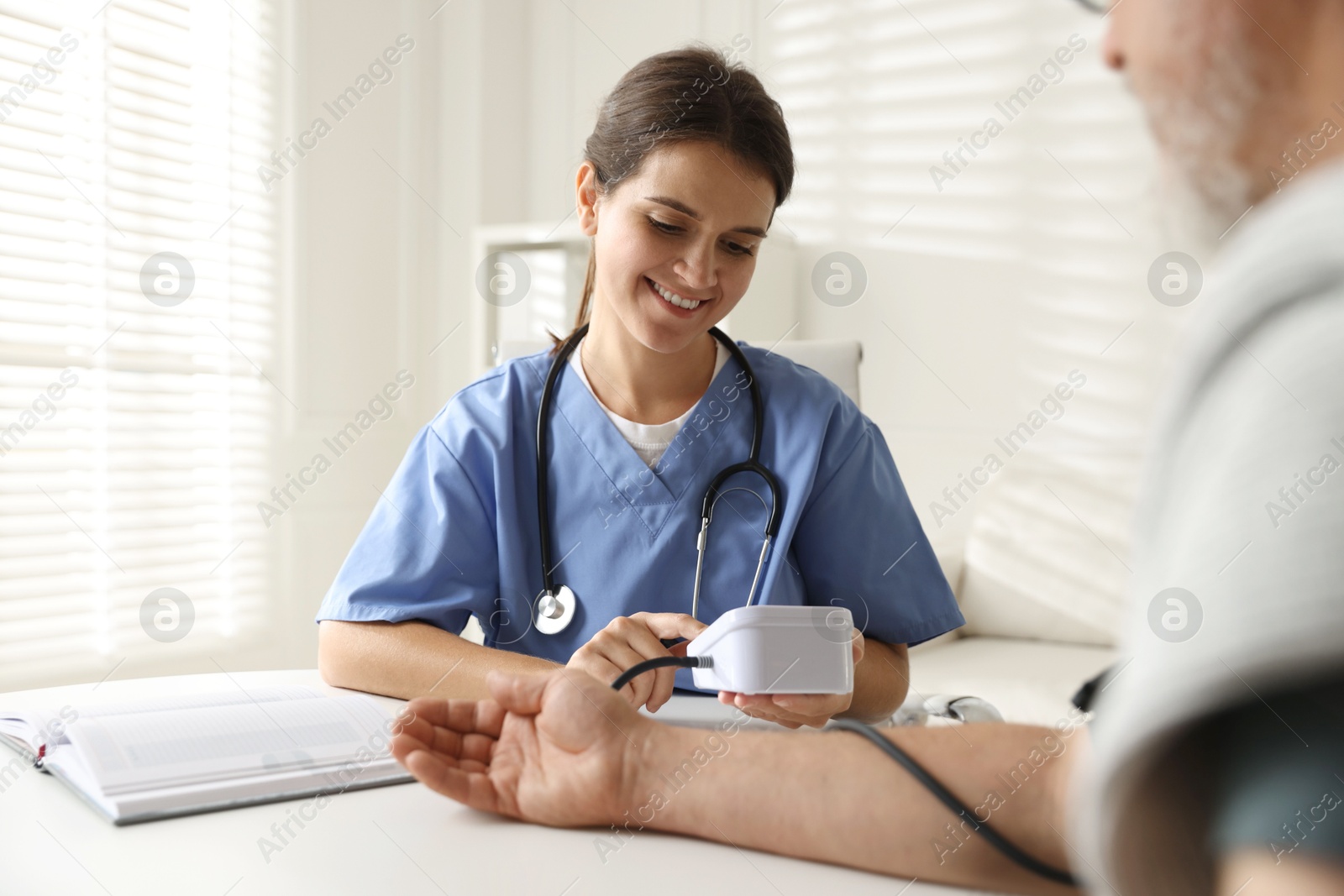 Photo of Doctor measuring patient's blood pressure at table indoors