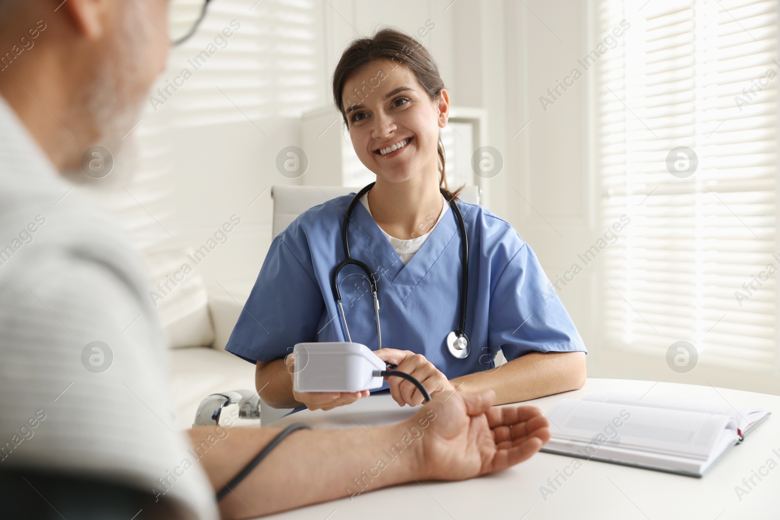 Photo of Doctor measuring patient's blood pressure at table indoors