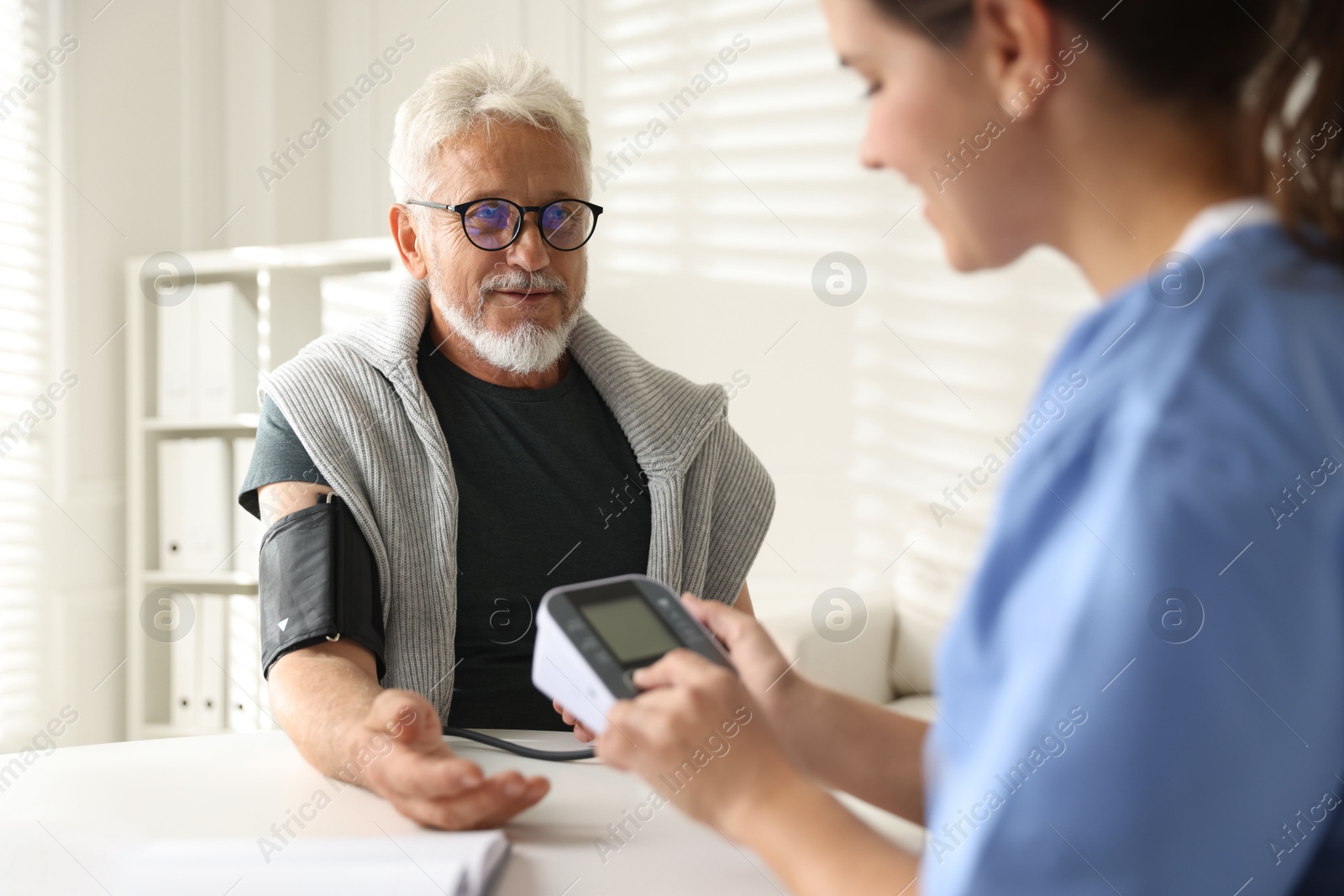 Photo of Doctor measuring patient's blood pressure at table indoors