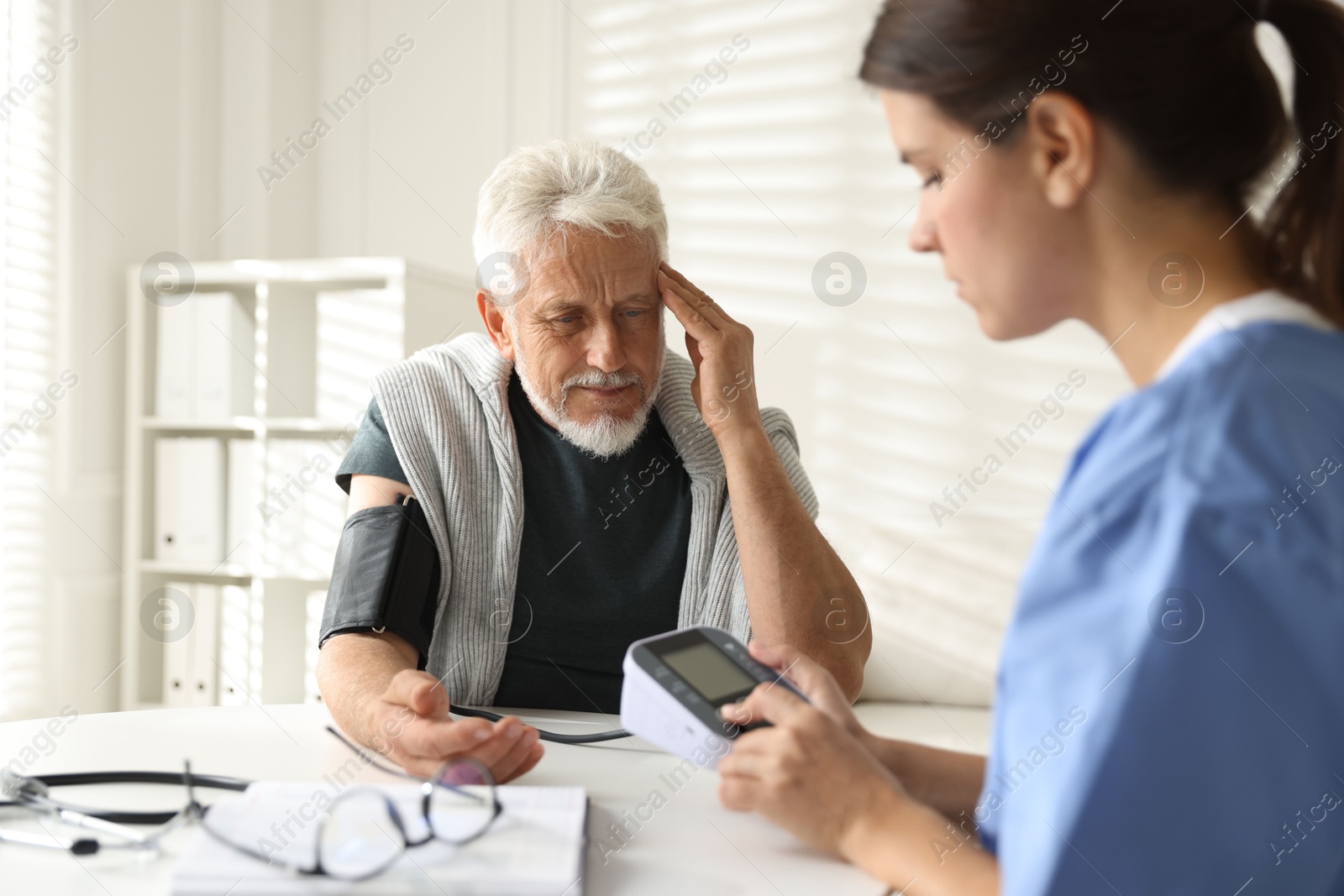 Photo of Doctor measuring patient's blood pressure at table indoors