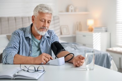 Photo of Senior man measuring blood pressure at table indoors