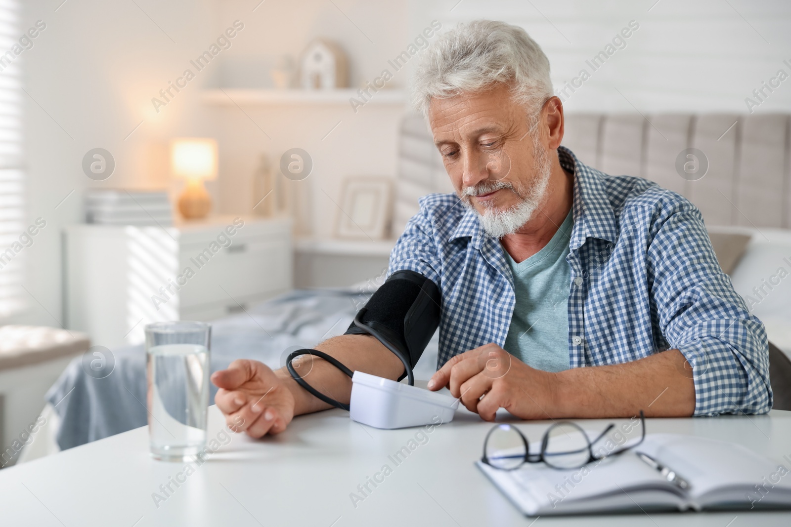 Photo of Senior man measuring blood pressure at table indoors