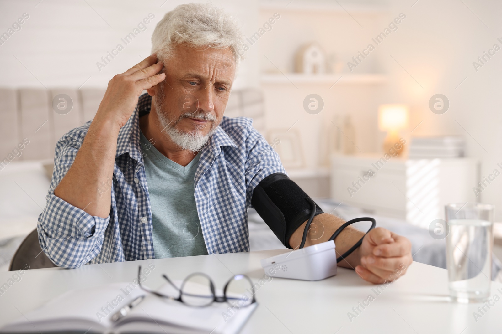 Photo of Senior man measuring blood pressure at table indoors