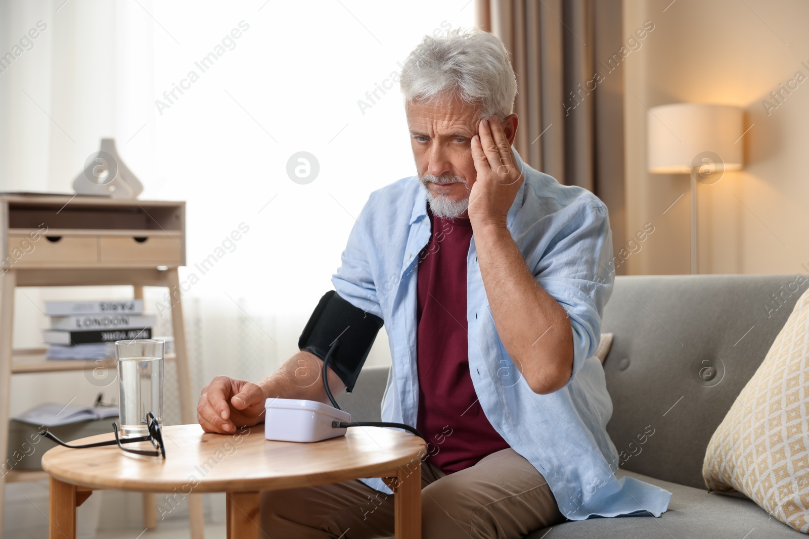 Photo of Senior man measuring blood pressure at table indoors