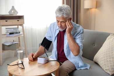 Photo of Senior man measuring blood pressure at table indoors