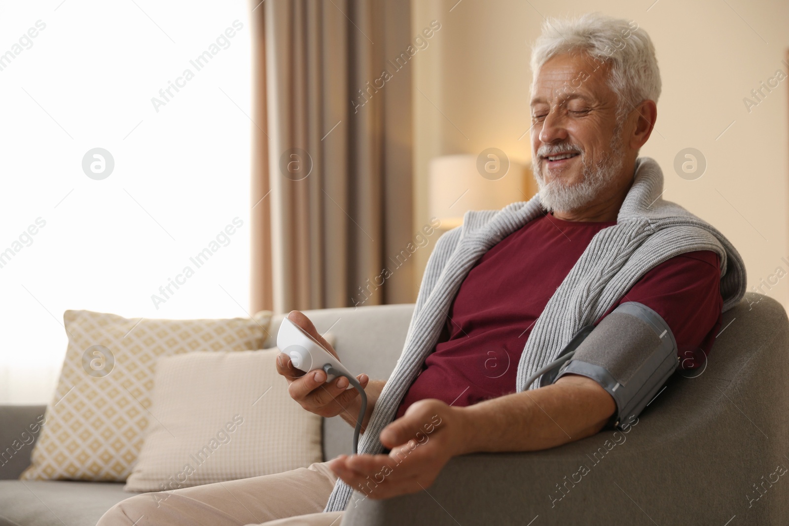 Photo of Senior man measuring blood pressure on sofa indoors