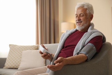 Photo of Senior man measuring blood pressure on sofa indoors