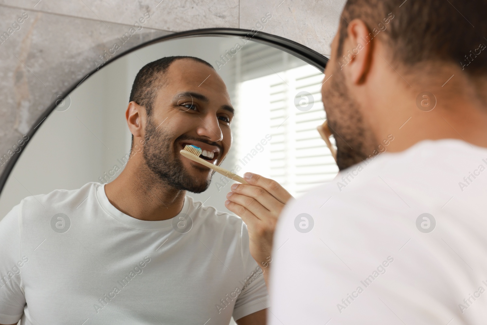 Photo of Smiling man brushing teeth near mirror in bathroom