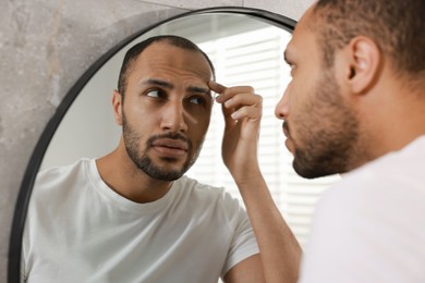 Photo of Worried man looking at mirror in bathroom