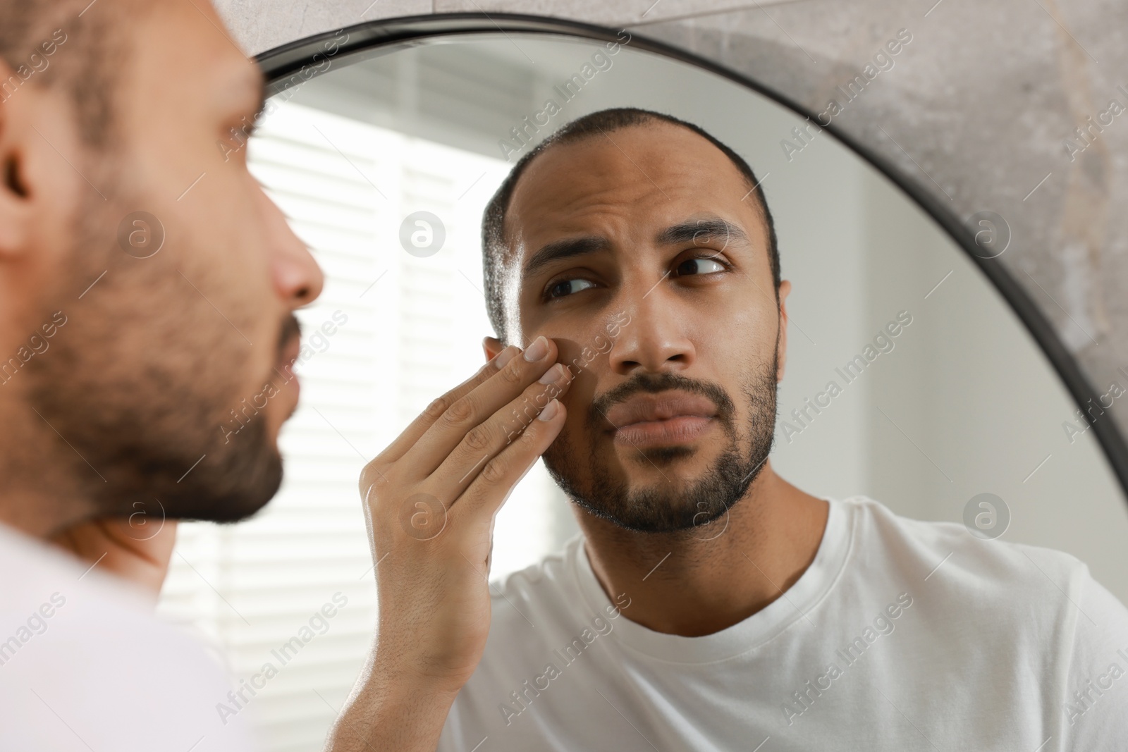 Photo of Worried man looking at mirror in bathroom