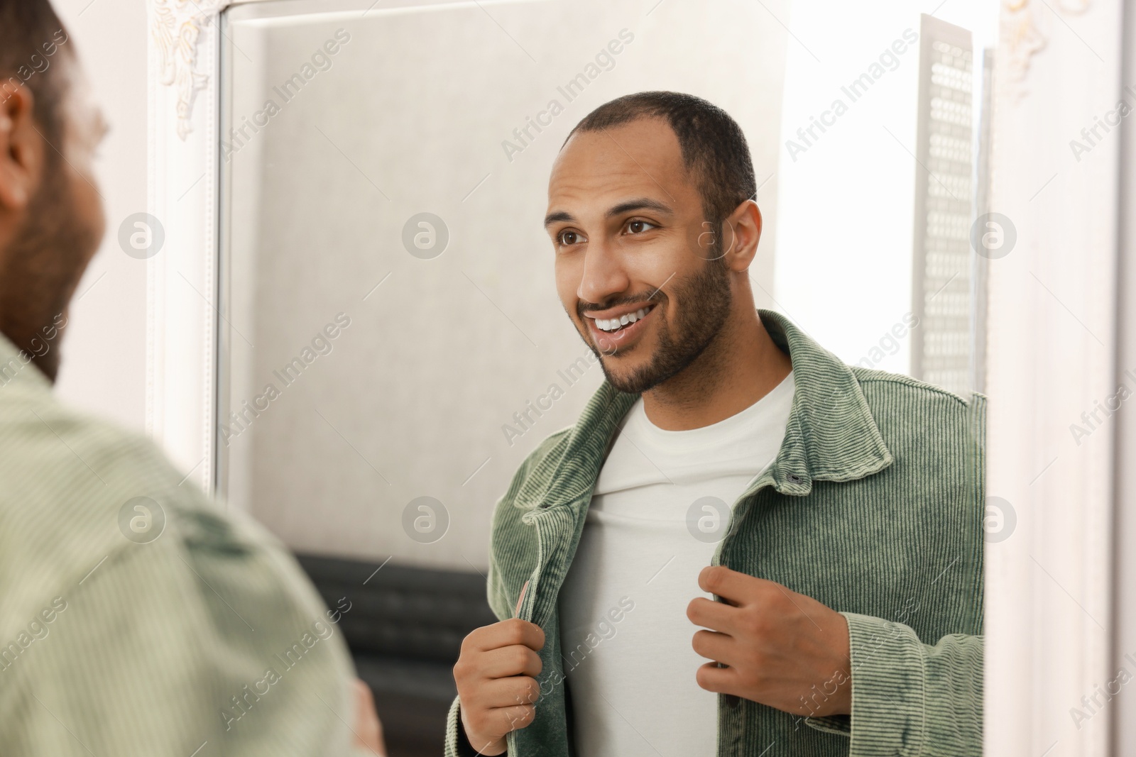 Photo of Smiling man dressing near mirror at home