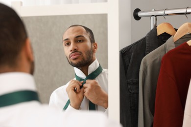 Photo of Handsome man adjusting necktie near mirror at home