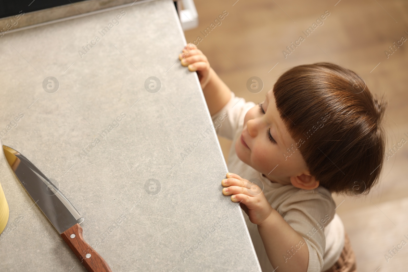 Photo of Little boy reaching towards knife on kitchen counter, above view. Dangerous situation