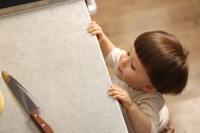 Photo of Little boy reaching towards knife on kitchen counter, above view. Dangerous situation