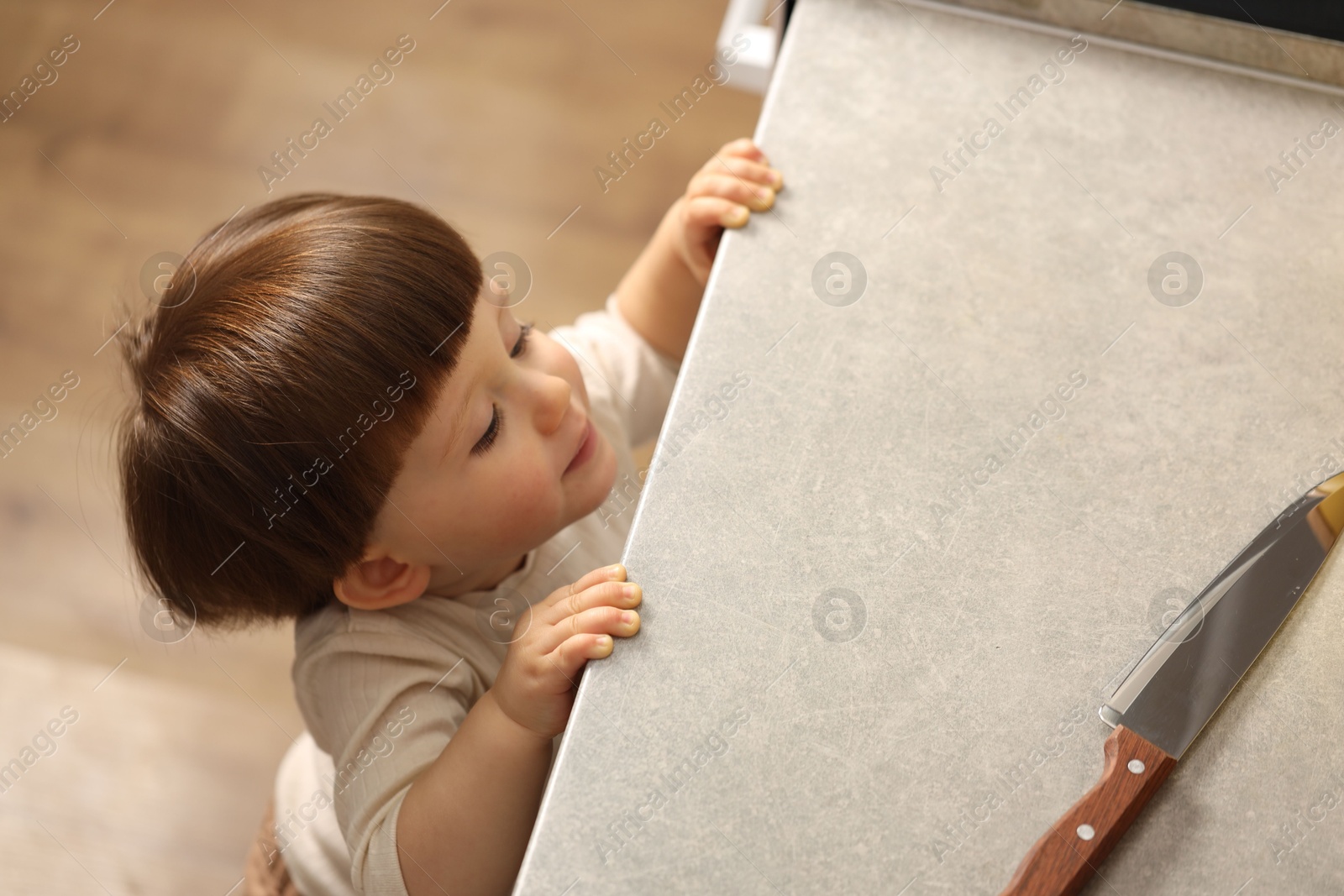 Photo of Little boy reaching towards knife on kitchen counter, above view. Dangerous situation