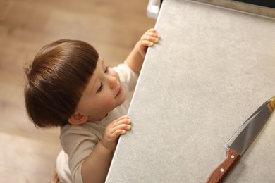 Photo of Little boy reaching towards knife on kitchen counter, above view. Dangerous situation