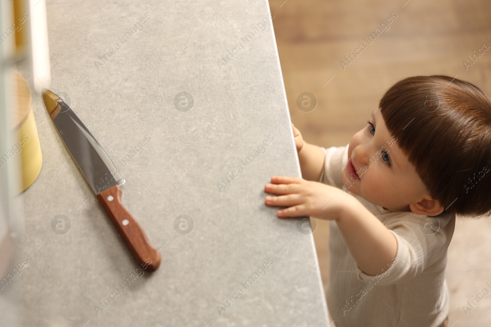 Photo of Little boy reaching towards knife on kitchen counter, above view. Dangerous situation