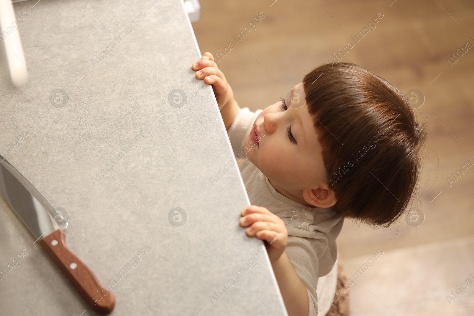 Photo of Little boy reaching towards knife on kitchen counter, above view. Dangerous situation