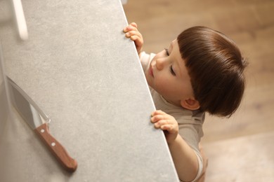 Photo of Little boy reaching towards knife on kitchen counter, above view. Dangerous situation