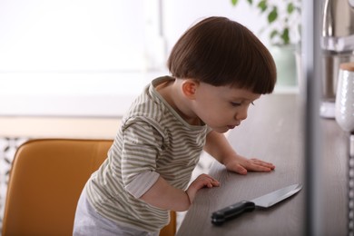 Photo of Little boy reaching towards knife on kitchen counter. Dangerous situation